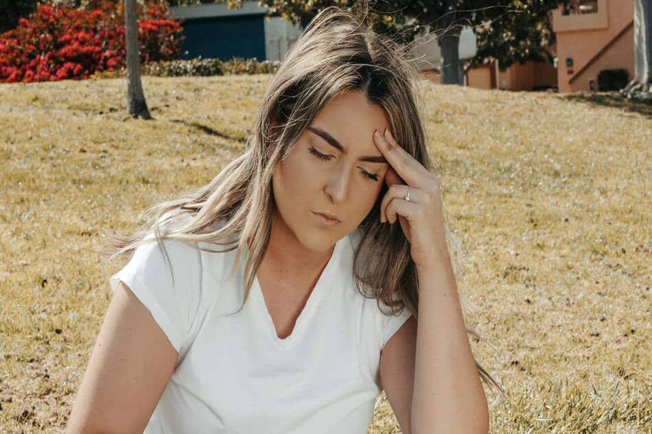 A woman sitting outdoors holding her head due to a migraine.