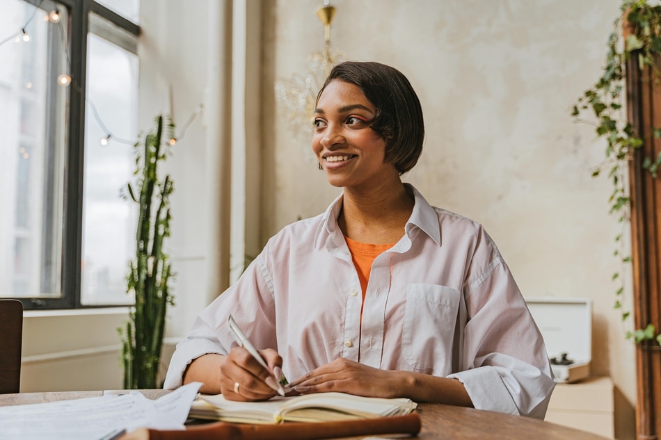 A woman holding a pen and looking away from her notebook.